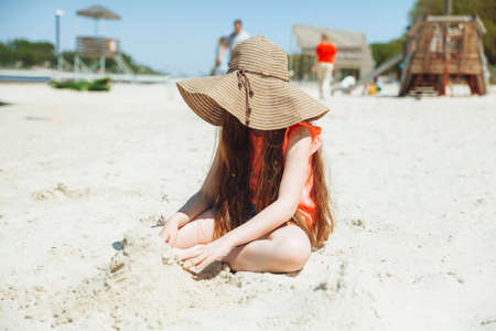 A 7-year-old girl plays in the sand on a city beach. vacation and rest. Playful active child on the beach in summer vacationの写真素材