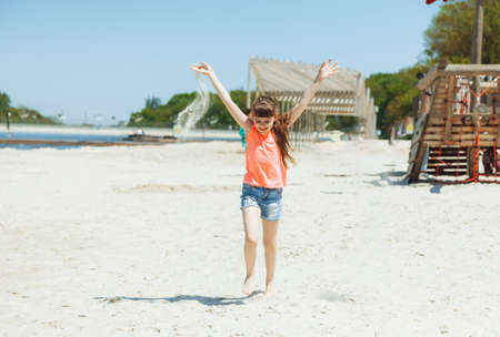 Happy little girl with long hair runs along the beachの写真素材