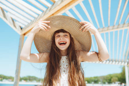 cute little girl in a hat smiles on the beach on a summer day. portrait of a girl on the beach.の写真素材