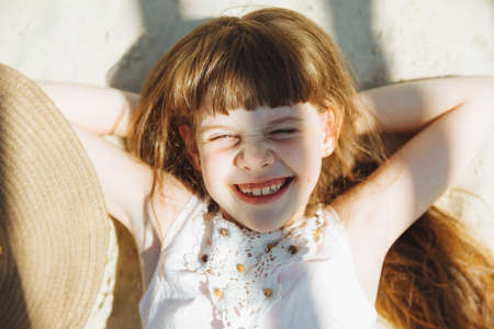 Summer, holidays and people concept - little girl in a straw hat sunbathing on a sandy beachの写真素材