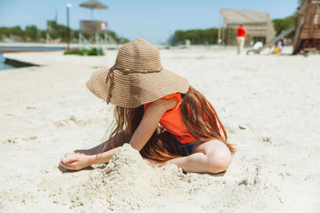 A 7-year-old girl plays in the sand on a city beach. vacation and rest. Playful active child on the beach in summer vacationの写真素材