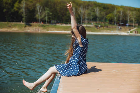 A little girl sits on a pier near the city lake outdoors. summer holidays