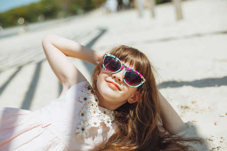 a little blonde girl in a straw hat lies on a sandy beach. girl sunbathing on the sandの写真素材