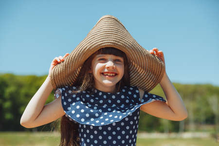 A cute little girl in a straw hat stands on a wooden bridge near the city lakeの写真素材