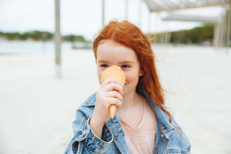 Happy little girl with red hair eats ice cream on the beach in summer. summer holidays