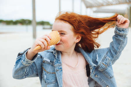 Happy little girl with red hair eats ice cream on the beach in summer. summer holidays