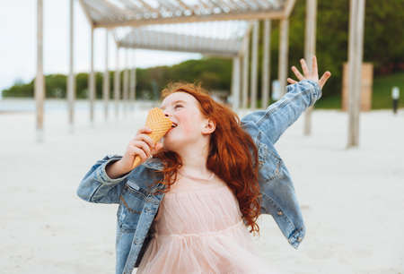 Happy little girl with red hair eats ice cream on the beach in summer. summer holidays