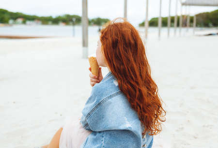 Happy little girl with red hair eats ice cream on the beach in summer. summer holidaysの写真素材