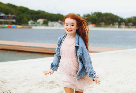 Happy little girl with red hair runs along the beach. child on the beach