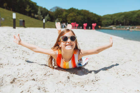 a little blonde girl in a straw hat lies on a sandy beach. girl sunbathing on the sandの写真素材