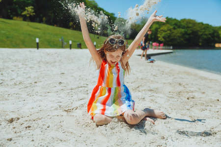 a little girl in a summer dress throws sand on the beach. summer holidaysの写真素材