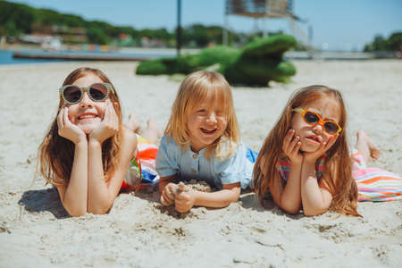 three happy children lie on the sand on the beach.a child with down syndrome with friends has fun on the beach.の写真素材