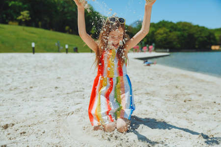 a little girl in a summer dress throws sand on the beach. summer holidays