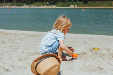 Cute happy blond boy playing with beach toys on the sandy city beach.の写真素材