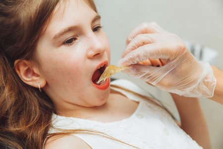 portrait of a little girl with an open mouth sitting in a dentist's chair while an orthodontist holds a plate on her teeth. Dentist puts a plate in a child's mouthの写真素材
