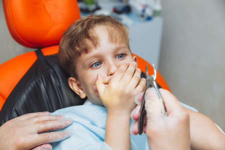 The boy is afraid of the dentist with forceps. The child is afraid to remove the tooth. The teenager...