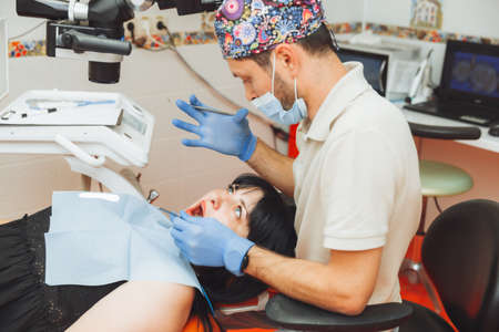 A male doctor examines the oral cavity of a young patient sitting in a dentist's chair in the office next to the dentist. the concept of healthy teeth.の写真素材