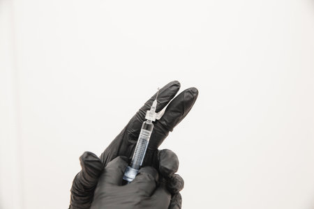 A close-up photo of doctors in disposable latex rubber gloves holding a syringe shows the injection...