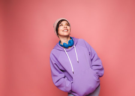 l young brunette girl in a lilac sweater and headphones poses in isolation on a pink background in...