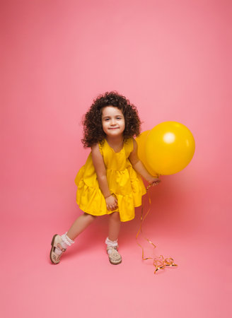 Portrait of a cheerful little girl isolated on a pink background, holding a bunch of colorful balloons, posing.の写真素材