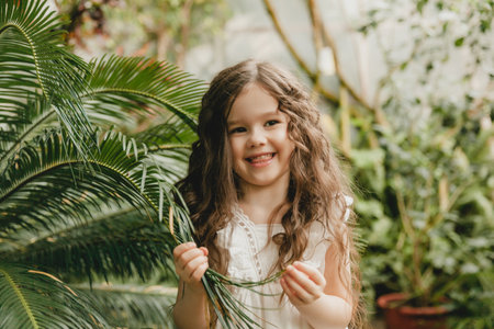 Little girl in the botanical garden. a girl in a white dress laughs near palm leaves.の写真素材