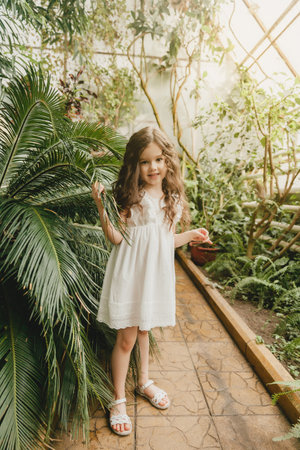 Little girl in the botanical garden. a girl in a white dress laughs near palm leaves.の写真素材