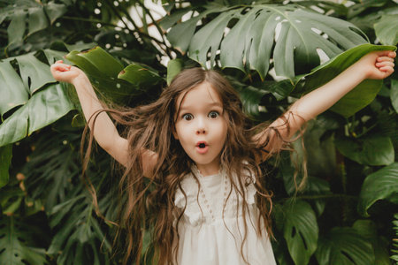 Little girl in a white dress in a botanical garden. a child stands near the leaves of Monstera.