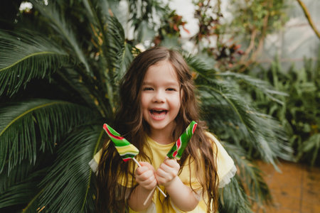 Cute little girl eating a watermelon shaped lollipop Child with lollipops in the botanical garden.の写真素材