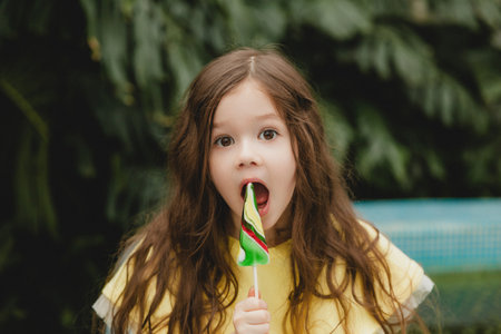 Cute little girl eating a watermelon shaped lollipop Child with lollipops in the botanical garden.の写真素材