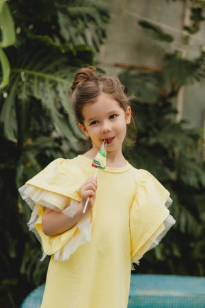 Cute little girl eating a watermelon shaped lollipop Child with lollipops in the botanical garden.の写真素材