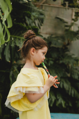 Cute little girl eating a watermelon shaped lollipop Child with lollipops in the botanical garden.の写真素材