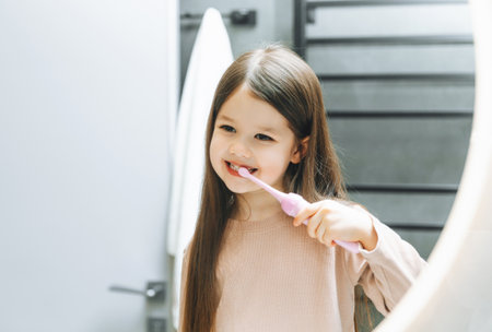 Happy little girl brushing her teeth in front of a bathroom mirror. Morning hygiene.の写真素材