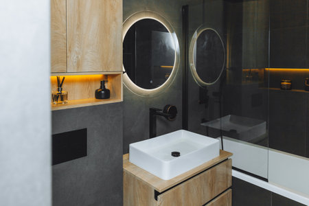 Modern bathroom with wooden countertop, shower, sink and round mirror.の写真素材