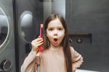 Happy little girl brushing her teeth in front of a bathroom mirror. Morning hygiene.の写真素材