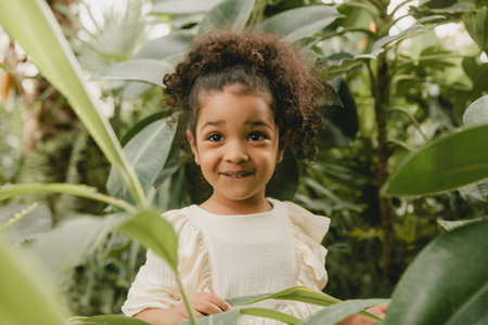 African American happy little girl, against the background of decorative leaves in the garden.の写真素材