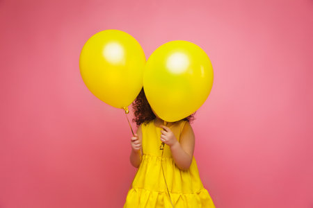 Portrait of a cheerful little girl isolated on a pink background, holding a bunch of colorful balloons, posing.の写真素材