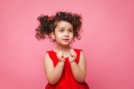 emotional portrait of a little girl in a red dress on a pink background.の写真素材