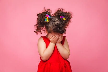 emotional portrait of a little girl in a red dress on a pink background.の写真素材