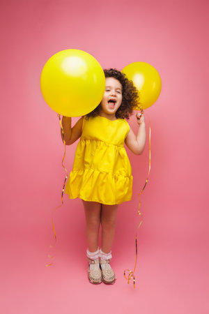 Portrait of a cheerful little girl isolated on a pink background, holding a bunch of colorful balloons, posing.の写真素材