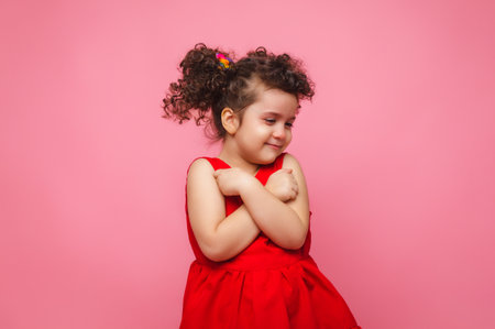emotional portrait of a little girl in a red dress on a pink background.の写真素材