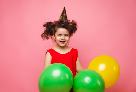 Portrait of a cheerful little girl isolated on a pink background, holding a bunch of colorful balloons, posing.の写真素材