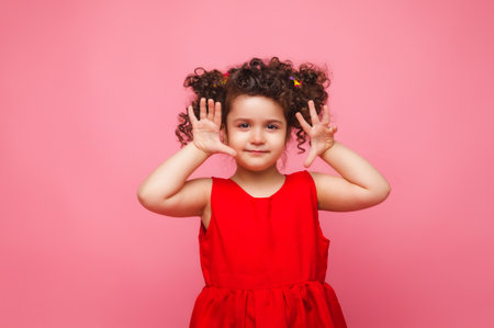 emotional portrait of a little girl in a red dress on a pink background.の写真素材