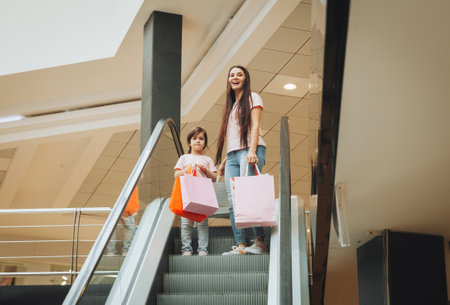 mother and little girl on the escalator in the mall. A young mother and her little child are shopping together.の写真素材