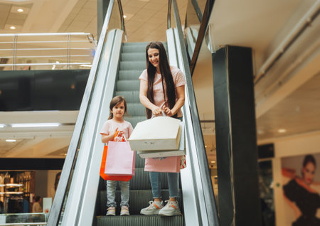 mother and little girl on the escalator in the mall. A young mother and her little child are shopping together.の写真素材