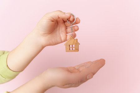 Close-up focus on keys with a house-shaped key chain in female hands, moving into a new apartment, creating the concept of a real estate bank mortgage loan transaction.の写真素材