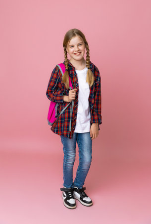 Full length smiling little schoolgirl 10-13 years old in casual denim clothes with backpack isolated...