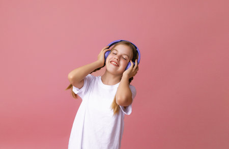 Photo of a cute funny young teenage girl in a jumper, headphones, dancing, enjoying music on a pink backgroundの写真素材