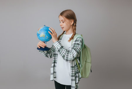 Caucasian young teenager schoolgirl student holding a globe on a gray background, isolated. happy...