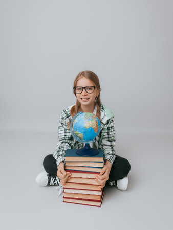 schoolgirl isolated on yellow background with globe. little girl in school uniform sitting on a yellow background, reading a book. blonde girl in school uniform on a yellow backgroundの写真素材