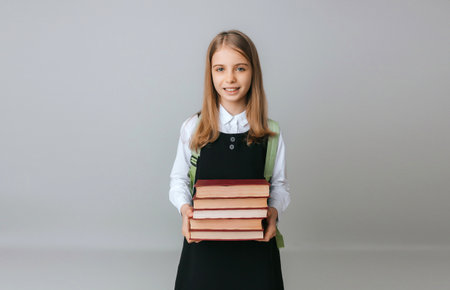 schoolgirl 11-13 years old holding heavy textbooks on gray studio background.back to school. education conceptの写真素材
